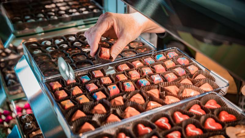 A chocolatier reaches into a display case filled with various chocolate treats in Saint Paul, MN.