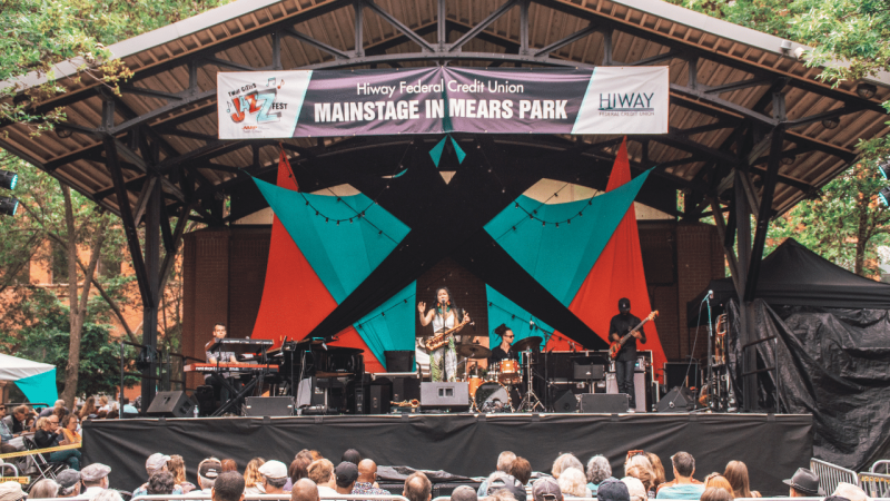 A band on stage at an ampitheatre in Saint Paul, MN with a sign that reads MAINSTAGE IN MEARS PARK.