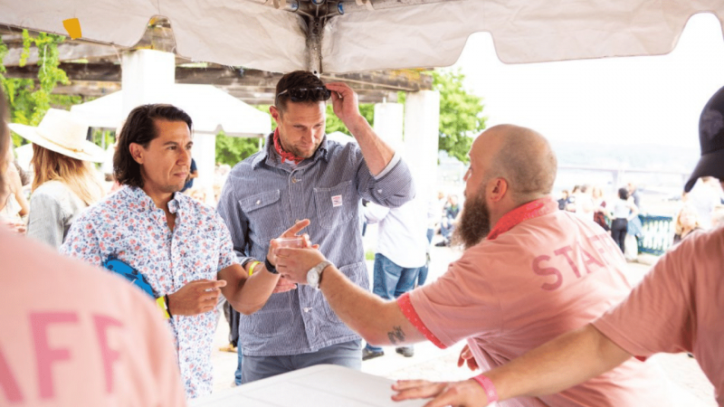 Two men are handed beverages from under a tent by a man in a pink shirt reading STAFF on the back in Saint Paul, MN.
