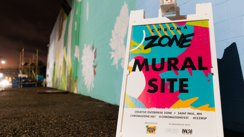 A sign in front of painted wall reading Chroma Zone Mural Site in Saint Paul, MN.